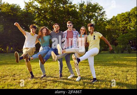 Lustige Gruppe von Freunden, die Spaß haben und herumtörnend Cancan im Park auf grünem Rasen tanzen. Stockfoto
