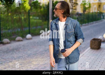 Überführung mittleren Alters Krise reifer Mann lehnte sich auf Straße Schild halten Tasse Kaffee. Erleben Kater mittleren Alters alkoholischen Mann trinken mit Papierbecher, um Alkohol zu verstecken. Psychologiekonzept. Stockfoto