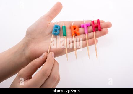 Farbe-Kerzen in der Hand auf Sticks schreiben die Wort Geburt Stockfoto