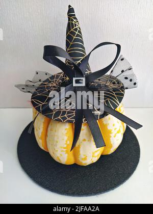 Natürlich reifer Kürbis mit einem eleganten Hexenhut mit Schleife und Schleier verziert. Halloween Hausdekoration Konzept Stockfoto