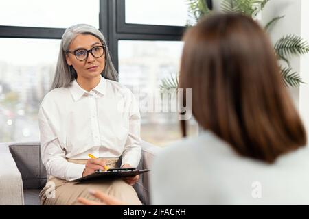 Reifer Senior Therapeut drückt einer verärgerten Patientin während der Therapiesitzung Unterstützung und Empathie aus. Konzept der psychischen Gesundheit Stockfoto