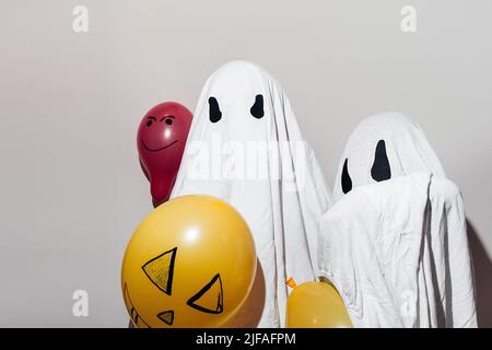 Frohe Halloween. Die Kinder kleideten sich in weißen Geisterkostümen und bemalten orangefarbene Ballons. Verschiedene Emotionen von Freude, Wut, Lachen. Festliche Dekoration, Partykonzept. Stockfoto