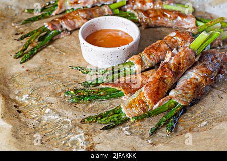 Gebackener grüner Spargel, eingewickelt in knusprigen Speck. Leichter Snack, Beilage (garniert). Stockfoto