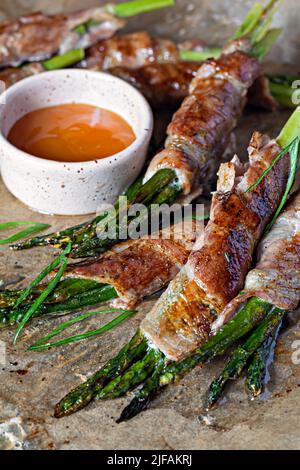 Gebackener grüner Spargel, eingewickelt in knusprigen Speck. Leichter Snack, Beilage (garniert). Stockfoto