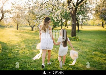 Glückliche Kindheit mit Mama. Die Tochter hält die Hand ihrer Mutter und läuft mit ihr durch den frühlingsblühenden Garten Stockfoto