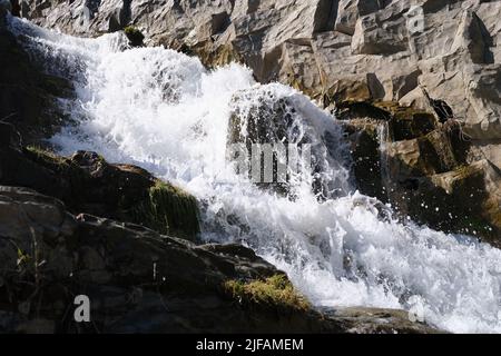 Wilder Gebirgsfluss mit kleinen Wasserfällen, die durch Steine fließen Stockfoto