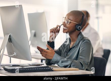Glücklicher, junger afroamerikanischer Callcenter-Telemarketing-Agent, der während der Arbeit an einem Computer in einem Büro mit einem Headset spricht. Selbstbewusste, freundliche Hündin Stockfoto