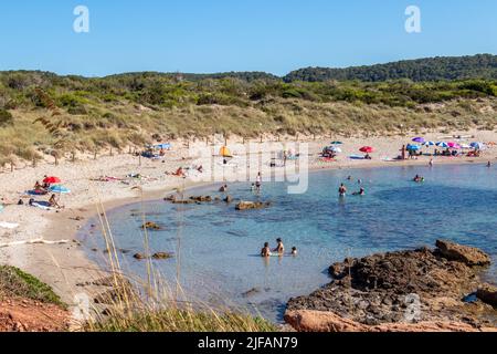 Menorca, Spanien - 30. Jun 2022: Menschen, die in den transparenten Gewässern der unberührten Bucht Algaiarens auf Menorca baden Stockfoto