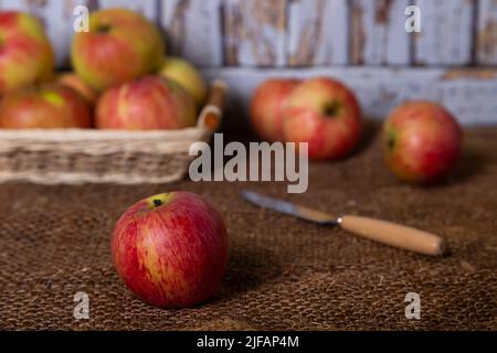 Reife Äpfel auf Sackleinen und in einem Korb. Rustikaler Stil, Nahaufnahme. Stockfoto