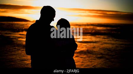 Silhouette liebevoll junges Paar teilt einen intimen Moment am Strand. Beleuchteter glücklicher Ehemann und Ehefrau genießen einen Sommertag am Meer. Sie Stockfoto