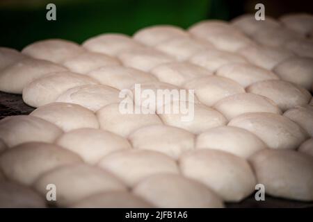 Bild von rohem Brotteig, geformt wie Brötchen, in der Gruppe, in einer Bäckerei, bereit zum Backen. Stockfoto