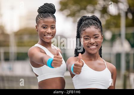 Portrait afroamerikanischer Tennisspieler mit Daumen nach oben. Glückliche Freunde unterstützen sich gegenseitig vor dem Tennistraben. Junge Tennisspieler feiern Stockfoto