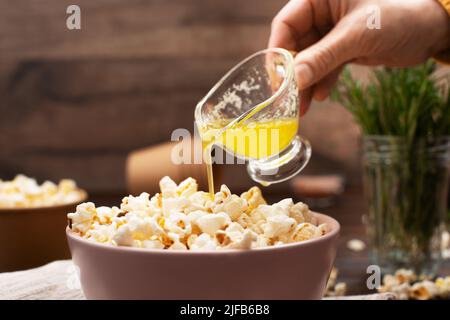 Geschmolzene Butter wird in einer Tonschüssel auf dem Küchentisch auf Popcorn gegossen Stockfoto