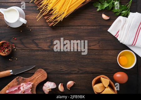 Zutaten für Pasta Carbonara. Traditionelle italienische Pasta Carbonara Zutaten Speck, Spaghetti, Parmesan und Eigelb, Knoblauch. Alter Tisch aus dunklem Holz Stockfoto