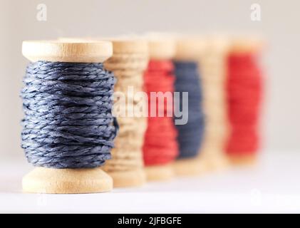 Viele Rollen aus farbigem Garn oder Faden Reihen sich in einer Reihe im Studio auf einem grauen Hintergrund isoliert an. Für die Herstellung von Textilien, Nähen Stockfoto