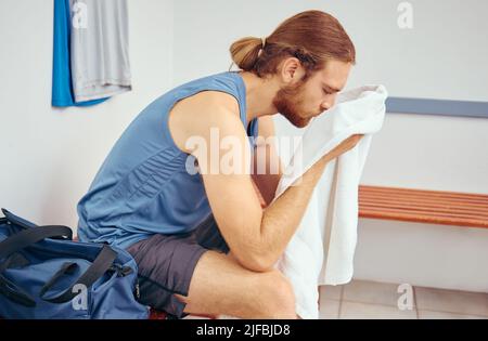 Kaukasischer Spieler, der sein Gesicht mit einem Handtuch abwischt. Müder junger Spieler, der nach einem Squash-Match sein Gesicht wischte. Profisportler, der eine Pause von ihm einlegte Stockfoto