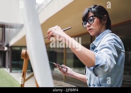 Junge Künstler Malerei Leinwand auf Staffelei im Freien in Park Stadt - Fokus auf Maler Frau Gesicht Stockfoto