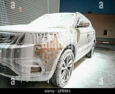 Auto in weißem Waschmittelschaum bei der Waschanlage. Stockfoto