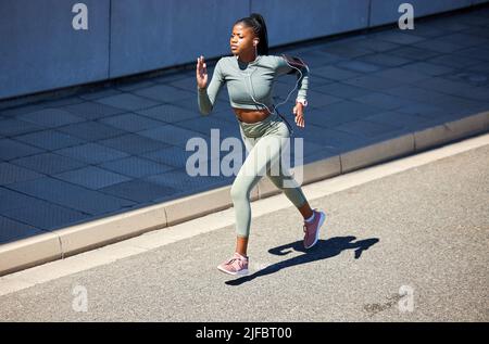 Fit und aktiv afroamerikanische Frau Musik über Kopfhörer hören und laufen allein in der Stadt. Schwarze Frau konzentrierte sich auf Fitness und Geschwindigkeit Stockfoto