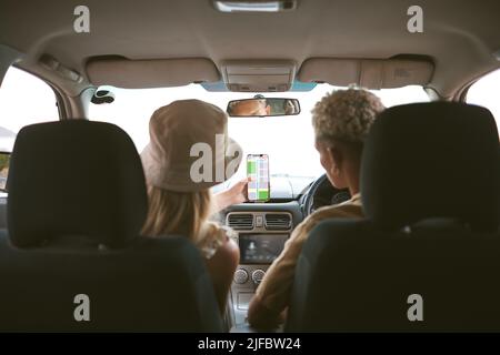 Rückansicht eines Rüden mit gemischter Rasse und seiner kaukasischen Freundin mit einem GPS-Smartphone, um sich im Auto zu einem Ort zu bewegen