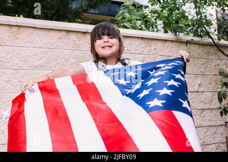 Das schwarzhaarige Mädchen hält und schwenkt eine Flagge der Vereinigten Staaten im Garten ihres Hauses. Konzept der Feier, Unabhängigkeitstag, Vereinigte Staaten von Amer Stockfoto