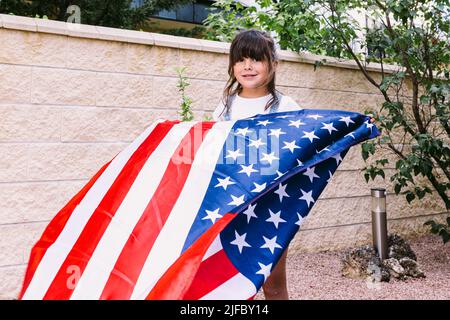 Das schwarzhaarige Mädchen hält und schwenkt eine Flagge der Vereinigten Staaten im Garten ihres Hauses. Konzept der Feier, Unabhängigkeitstag, Vereinigte Staaten von Amer Stockfoto