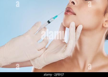 Schöne junge Mischrasse Frau bekommen plastische Chirurgie Botox Injektion in ihre Lippen. Attraktive weibliche isoliert im Studio vor blauem Hintergrund Stockfoto
