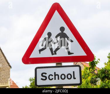 Ein Straßenschild warnt die Fahrer, dass Kinder die Straße überqueren könnten, in der Nähe einer Schule in Großbritannien. Stockfoto