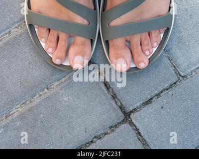 Frau Füße in Sandalen stehen auf Pflasterplatten. Nahaufnahme Stockfoto