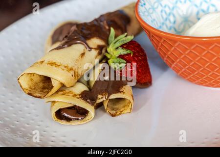 Gerollte Crepes mit Schokolade Haselnuss mit einer Erdbeere und einer Seite von Creme fraiche Schlagsahne Belag. Stockfoto