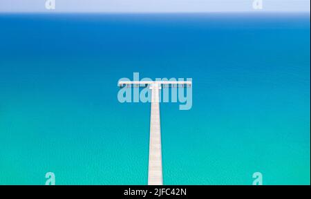 Weißer hölzerner Pier zum ruhigen blauen Meer, minimalistische Landschaft. Drohnenansicht von oben Stockfoto