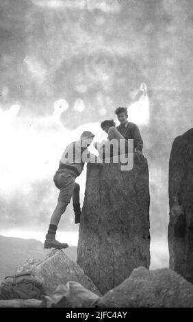 1952, historische, drei männliche Wanderer auf der Spitze des Berges von Tryfan, Snowdonia, Wales, mit zwei sitzen auf einem der beiden Zwillingsmonolithen von Adam und Eva (Sion a Sian in Wlesh) ein Paar Felsen drei Meter hoch. Stockfoto