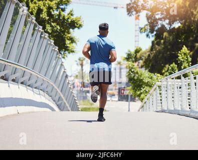 Rückansicht fit athletischen Mixed-Race-Mann läuft über eine Brücke in der Stadt für Fitness. Junger hispanischer Mann im Freien für ein Cardio-Training während des Tages Stockfoto
