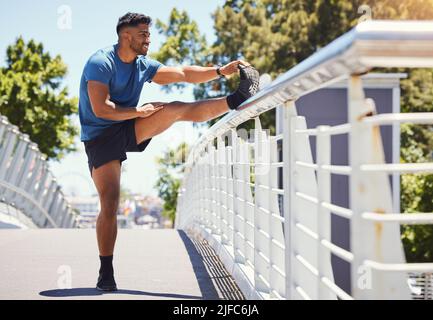 Fit athletischen Mixed-Race-Mann Stretching auf einer Brücke in der Stadt während seines Trainings. Junger hispanischer Mann, der an einem sonnigen Tag im Freien Aufwärmübungen macht Stockfoto