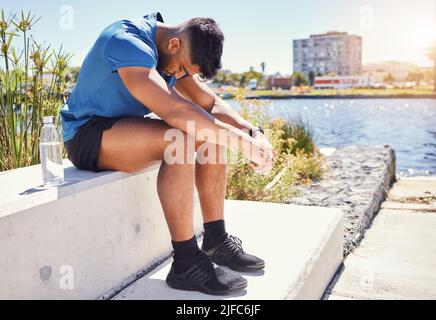 Ein junger Mann mit gemischter Rasse sitzt und macht eine Pause vom Training draußen. Übung hilft bei Depressionen und Angstzuständen. Hispanischer Mann schaut Stockfoto