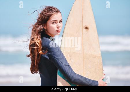 Porträt einer jungen kaukasischen Frau, die im Urlaub ein Surfbrett am Strand hält. Schöne Frau genießen das Wochenende und bleiben fit und mit ihr Stockfoto