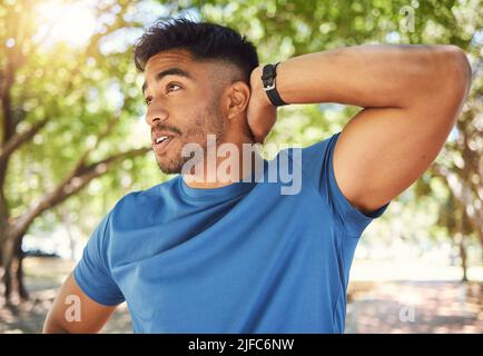 Ein sportlicher Mann lächelt, während er während eines Trainings im Park seine Arme streckt. Hispanischer Mann, der an einem sonnigen Tag im Freien Aufwärmübungen macht Stockfoto