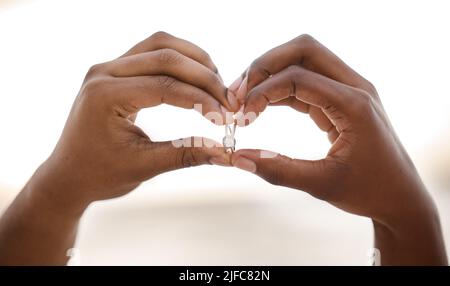 Nahaufnahme der Hände eines afroamerikanischen Mannes, der eine Herzform macht, während er einen Ring hält. Der Mann macht mit seinen Händen eine Herzgeste, während er eine zeigt Stockfoto