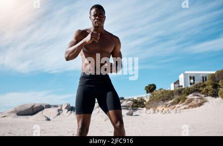 Ein hübscher junger afroamerikanischer Athlet, der am Strand trainieren kann. Dedizierter Black man Shadow Boxing während des Trainings im Freien auf dem Sand Stockfoto