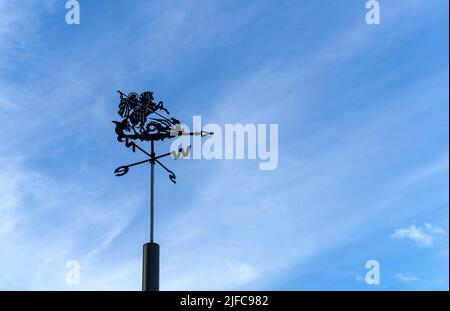 Wetterfahne, die die Richtung des Windes gegen den klaren blauen Himmel zeigt. Wetterfahne aus Metall mit Fahrer-Silhouette. Stockfoto