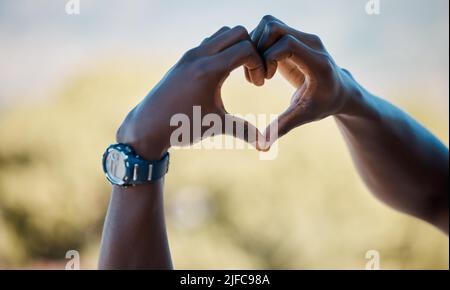 afroamerikanischer Athlet, der mit Händen und Fingern eine Herzform formt, um Liebe zu verbreiten. Hände eines frichtigen Mannes, der eine Uhr trägt, um seinen Fortschritt zu verfolgen Stockfoto