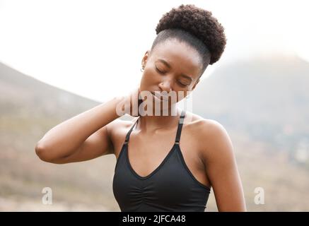 Junge afroamerikanische Frau, die unter Nackenschmerzen leidet, während sie draußen in der Natur arbeitet. Unglückliche junge Frau, die ihren Hals vor Schmerzen hielt Stockfoto