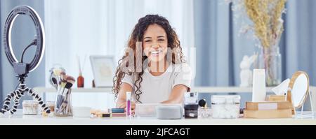 Eine hispanische Frau, die mit ihrem Telefon ein Make-up-Tutorial für ihren Beauty-Blog aufzeichnete, während sie zu Hause saß. afroamerikanische Influencerin live Stockfoto