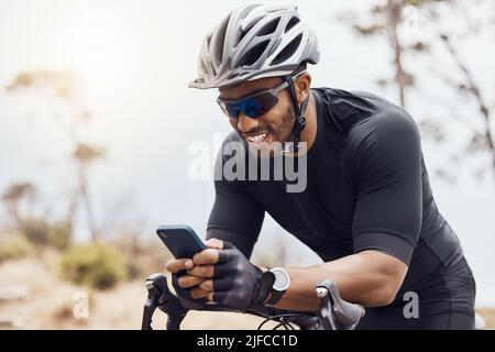 Lächelnder Radler, der sein Smartphone benutzt, während er auf seinem Fahrrad sitzt. Fit Sportler lächelnd und mit dem Handy beim Radfahren im Freien Stockfoto
