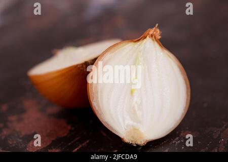 Eine halbierte weiße Zwiebel mit Haut auf, vor einem Hintergrund aus schwarzem Metall. Stockfoto