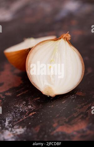 Eine halbierte weiße Zwiebel mit Haut auf, vor einem Hintergrund aus schwarzem Metall. Stockfoto