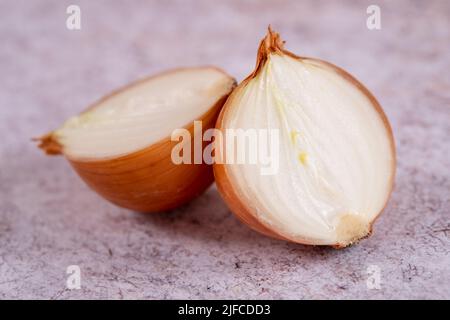 Eine halbierte weiße Zwiebel mit Haut auf, vor einem Hintergrund aus weißem Stein. Stockfoto