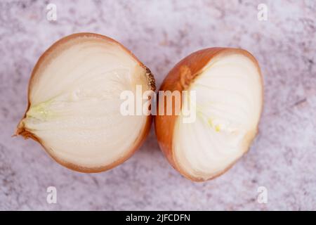 Eine halbierte weiße Zwiebel mit Haut auf, vor einem Hintergrund aus weißem Stein. Stockfoto