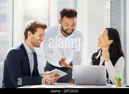 Eine Gruppe von glücklichen jungen, vielfältigen Kollegen, die gemeinsam an Unternehmensplänen in einem Bürovorstandssaal arbeiten. Gemischtes Rennen Geschäftsmann zeigt auf Laptop, während Stockfoto