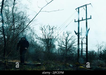 Eine gruselige dämonische Figur mit leuchtenden Augen. An einem stürmischen Wintertag in einem beängstigenden Wald auf die Kamera zu gehen. Mit einem Grunge, Textur bearbeiten. Stockfoto